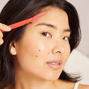 Model using a Kitsch Cherry Blossom Dermaplaner on her cheek for gentle facial exfoliation