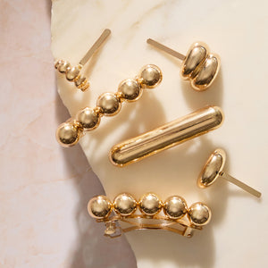 A set of kitsch gold-toned barrettes and hair pins arranged on a light marble surface