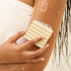 Hand applying lathered KITSCH Rice Water Protein Restoring Face & Body Wash Bar to arm in shower — in-use lifestyle shot with suds and lather — Hydrolyzed Rice Protein & Niacinamide Infused — For rough, irritated, & dry skin