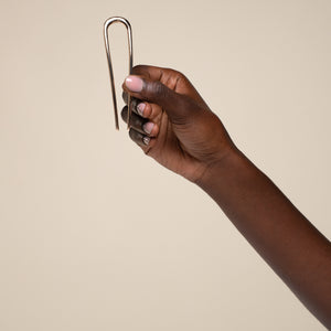 Hand holding kitsch gold mini metal clip against a beige background