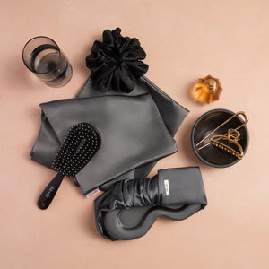 KITSCH Charcoal Contour Pillow Eye Mask — charcoal eye mask styled with a satin pillowcase, scrunchie, brush and gold claw clip on a peach surface — breathable memory foam keeps you cool and comfy all night long — a full satin sleep set
