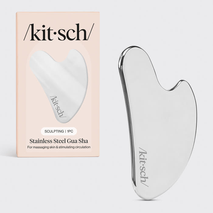 Kitsch Stainless Steel Gua Sha tool lying flat on marble surface showing curved edges