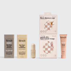 Kitsch hair care products including shampoo, conditioner, shower cap, and hair towel wrap on a gray background